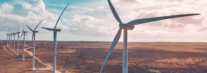 A drone shot of a line of wind turbines on a renewable energy farm; photo via Rabbi Shasha/Unsplash.