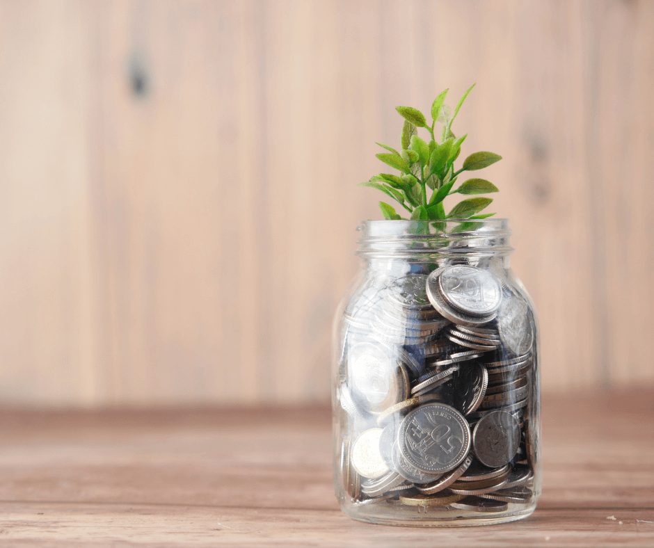 A small green plant sits on a glass jar full of coins.