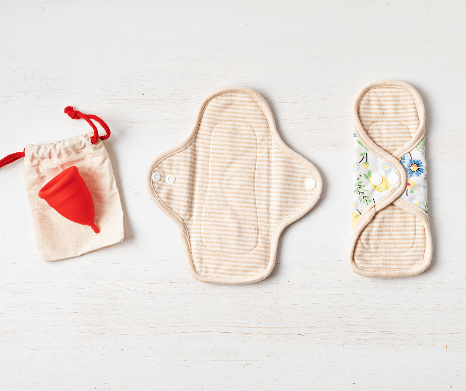 A red menstrual cup and two reusable sanitary pads are lined up on a white background.