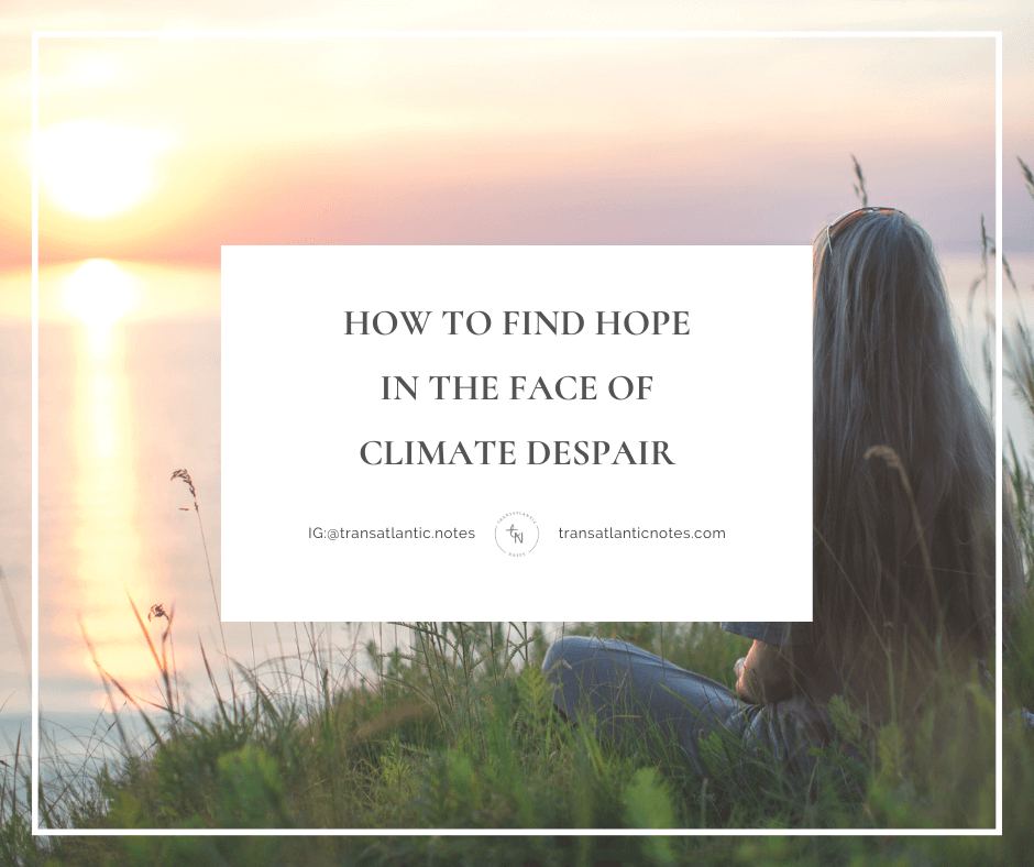 A young woman sits on the grass of a slight green hill, overlooking the sun setting in the distance.