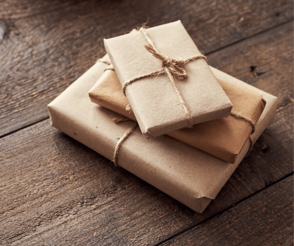 A pile of presents wrapped in brown recycled paper on a rustic wooden table.