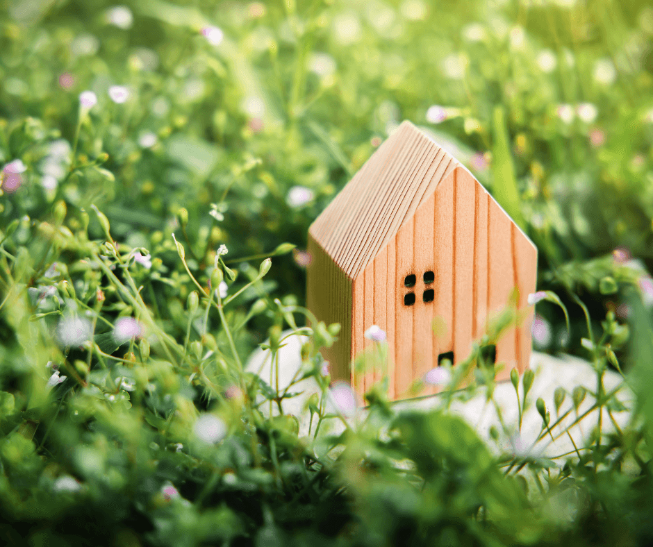 A small model of a wooden house on green grass that signifies the concept of living in harmony with nature.