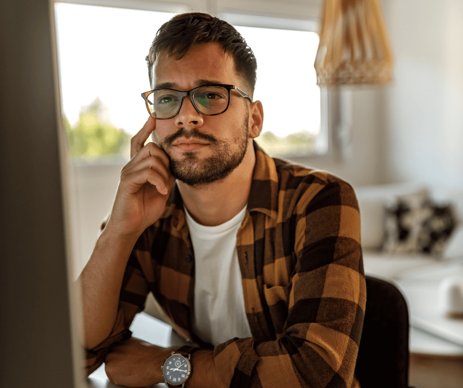A casually dressed man sits at his desk reading something on his computer.