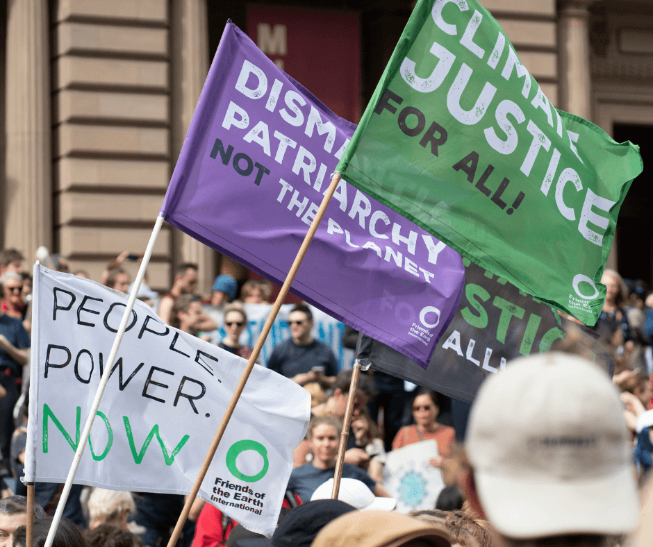 People marching for climate action hold up signs from Friends of the Earth calling for climate justice.