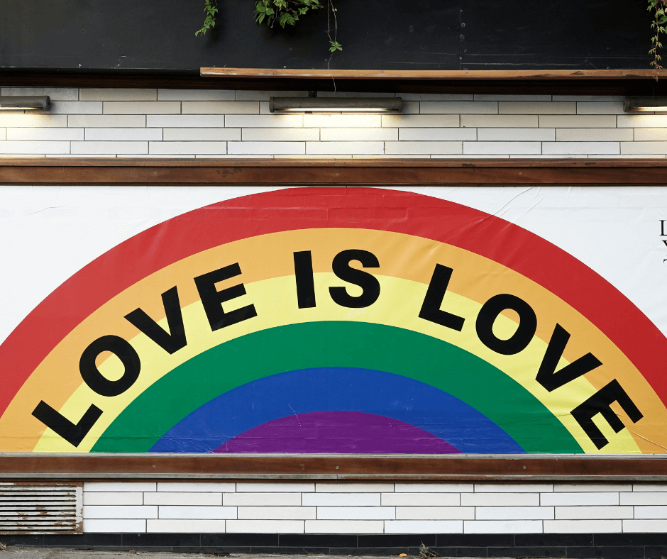 A colourful mural on a white tiled wall features a large rainbow with the words 'LOVE IS LOVE' written in bold black letters across the arches.