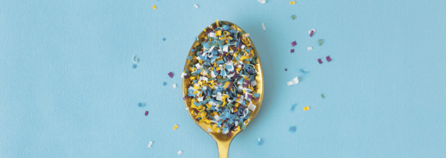 A pile of microplastics on a gold spoon against a light blue background; photo via Elena Sakhnenko/Canva.