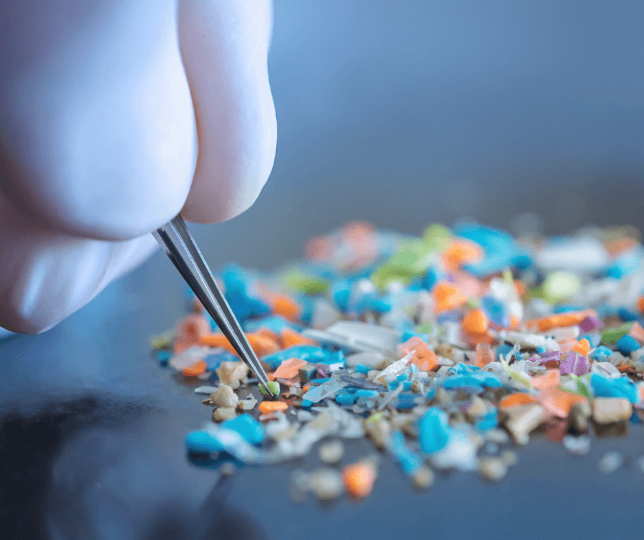 Close-up shot of the fingers of a person with medical gloves on holding tweezers inspecting a small pile of microplastics; only their fingers are visible.