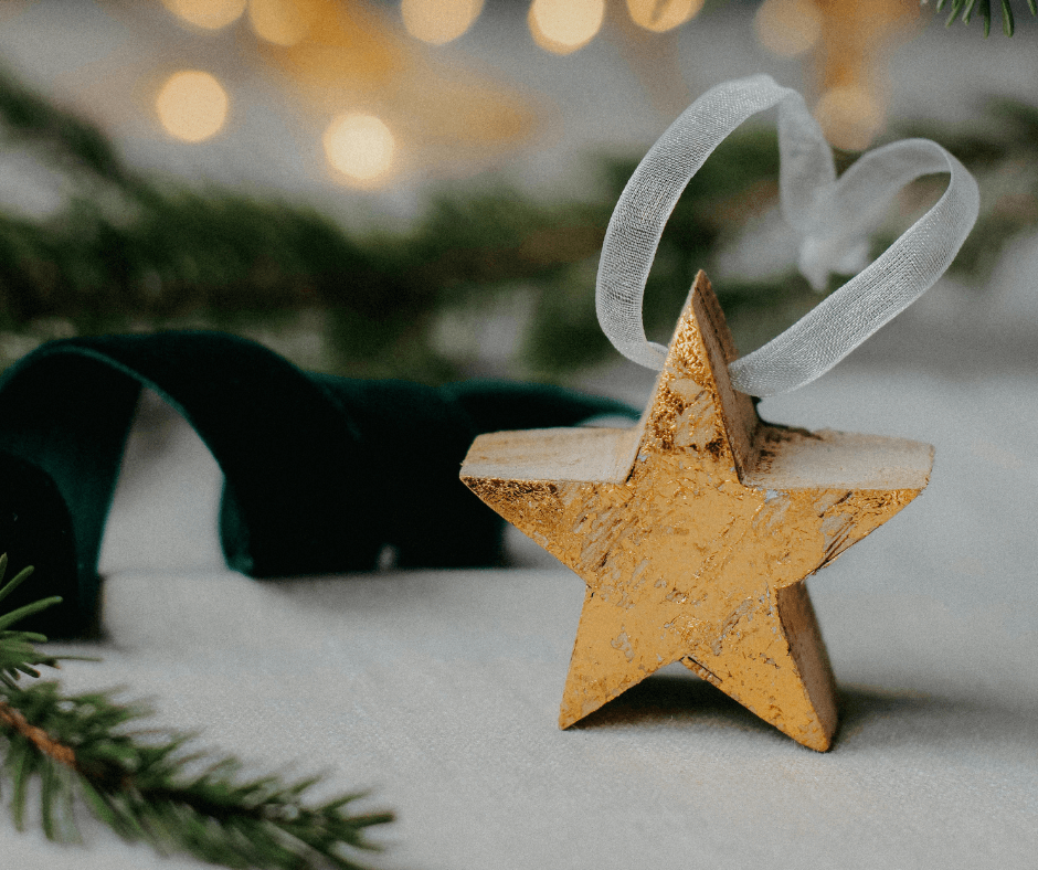 A close-up of a star-shaped golden holiday tree ornament made of wood with a white ribbon on top.