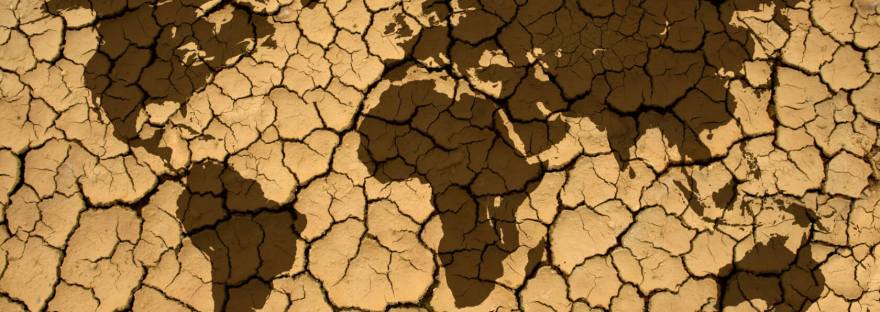 World map silhouette over cracked, dry earth, symbolizing global warming and drought.