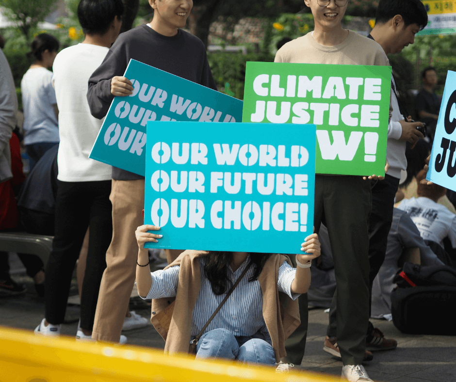 Youth climate activists hold bright blue and green protest signs reading "Our World, Our Future, Our Choice" and "Climate Justice Now" at an outdoor rally.